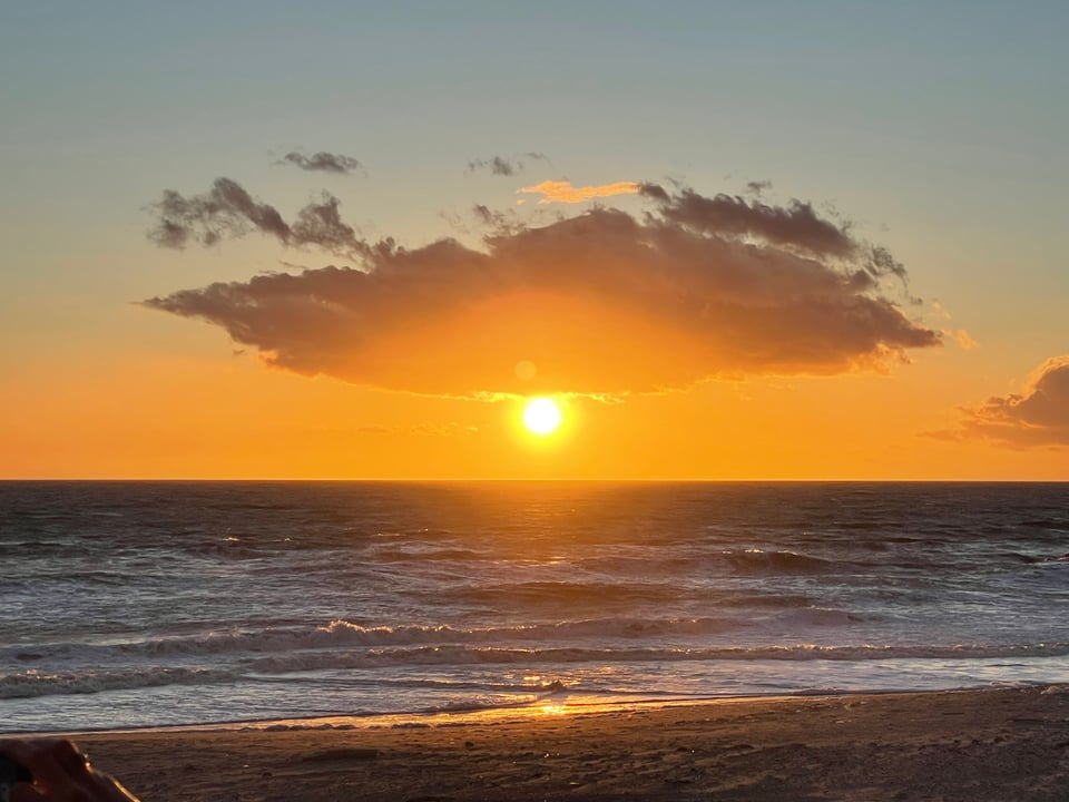 A sunset over rough water, a large cloud like an eyebrow makes the sun look like a testy eye