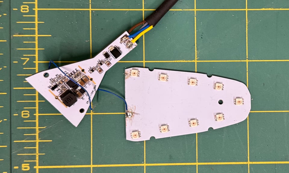 A turn signal circuit board, cut in half on a workbench, with wires soldered to both halves.