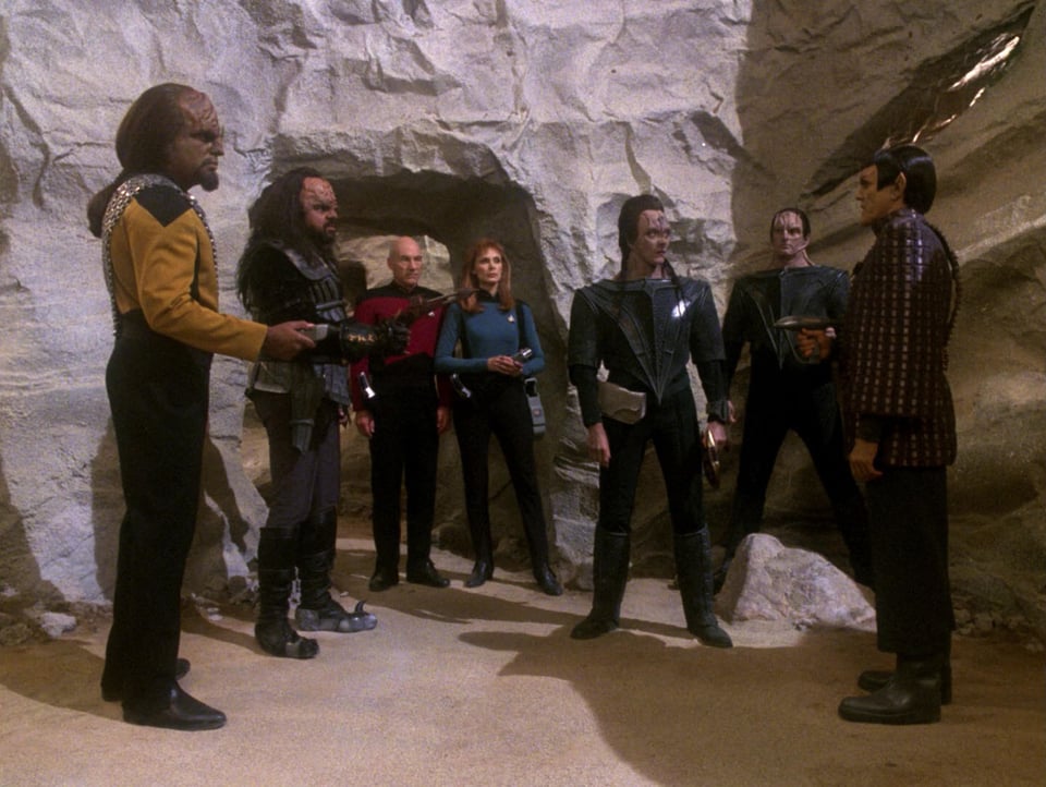 Klingons, Cardassians, Romulans, and Worf point weapons at each other. Picard and Crusher look on.