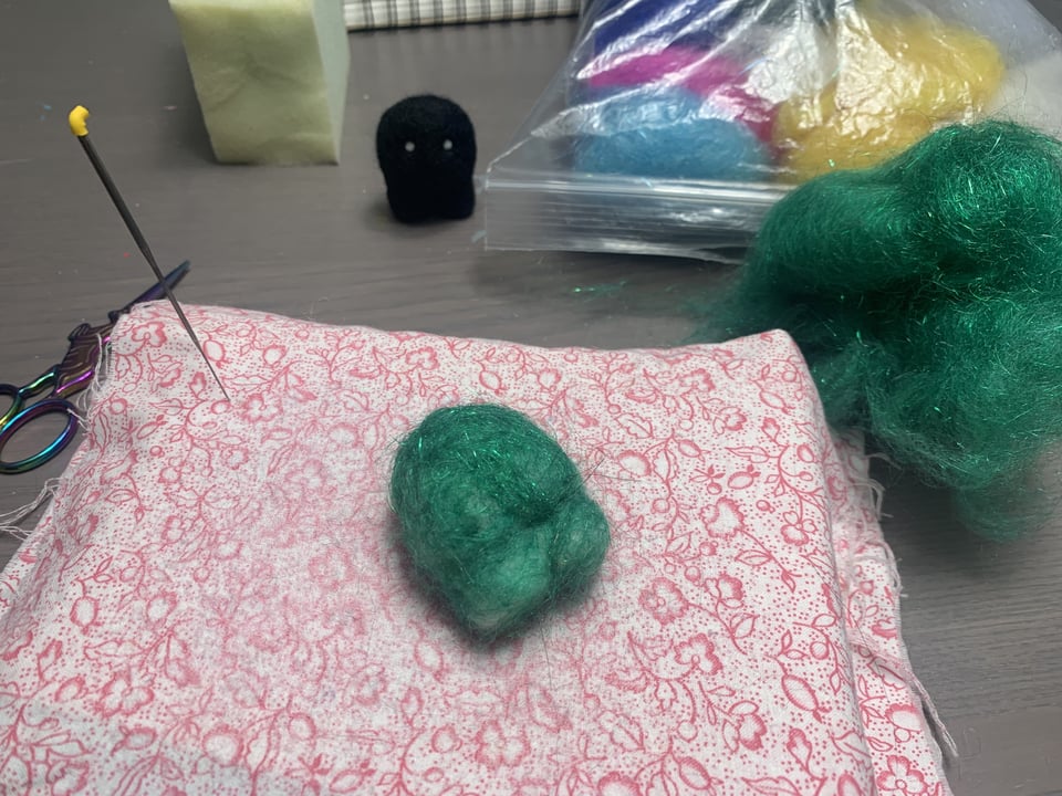 needle felting pad with a needle stuck in it and two in-progress felties nearby.