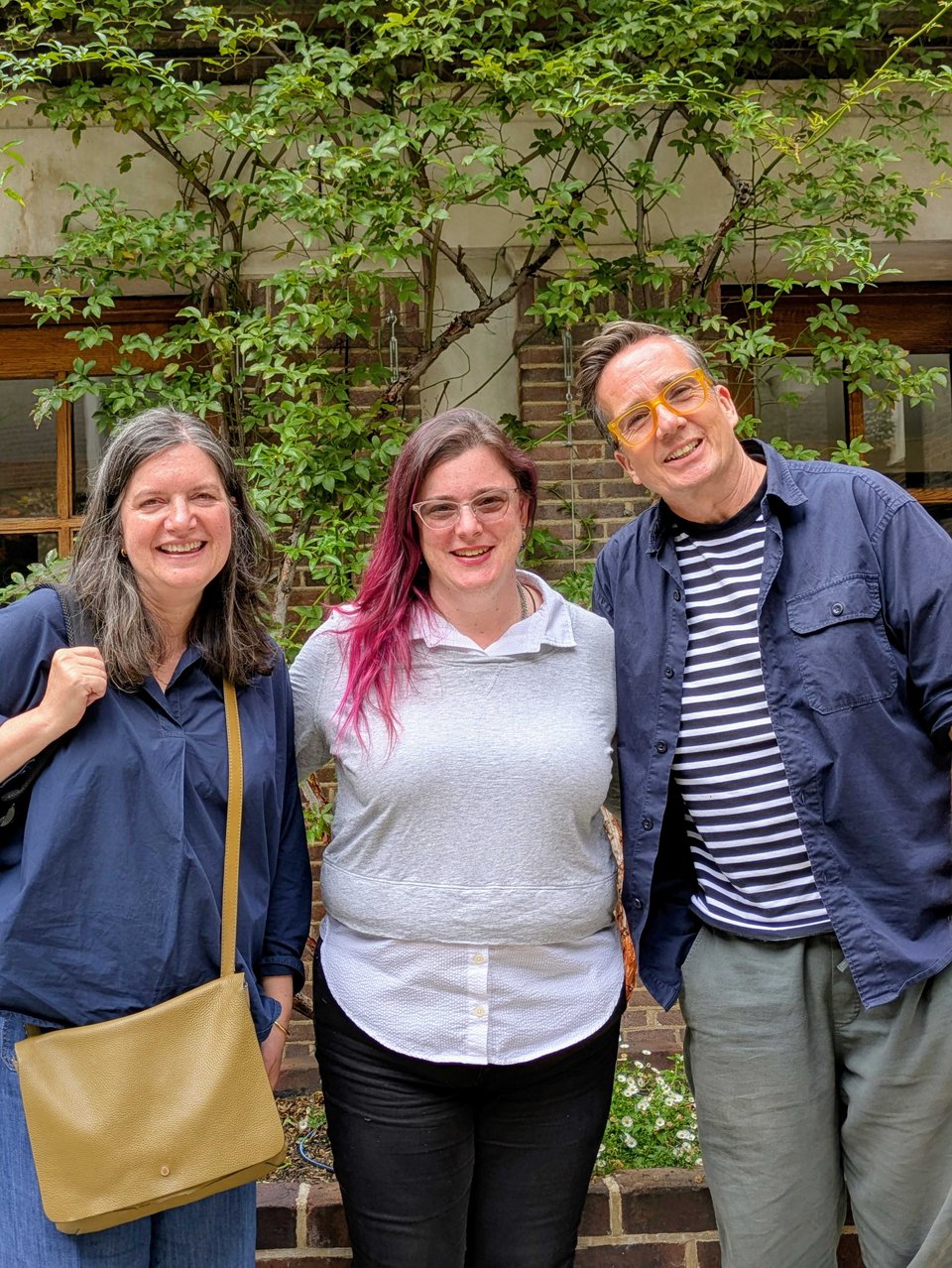 Meredith stands between Suzanne and Richard, and all three of them are smiling. They are in a garden in front of a tree.