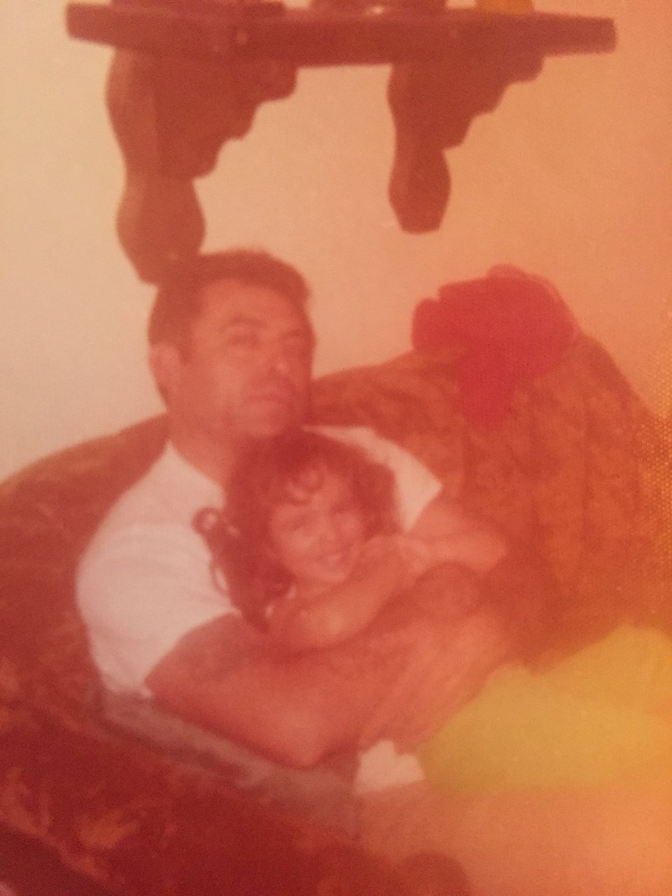  a very old photo of me and my father. I'm about 3 years old and he's sitting on a couch holding me tight in his arms. I'm smiling, probably laughing.