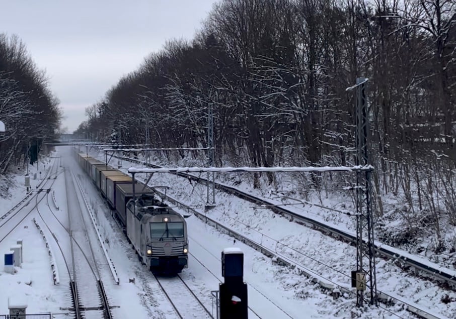 A train moving on snow covered tracks blowing snow dust in its wake