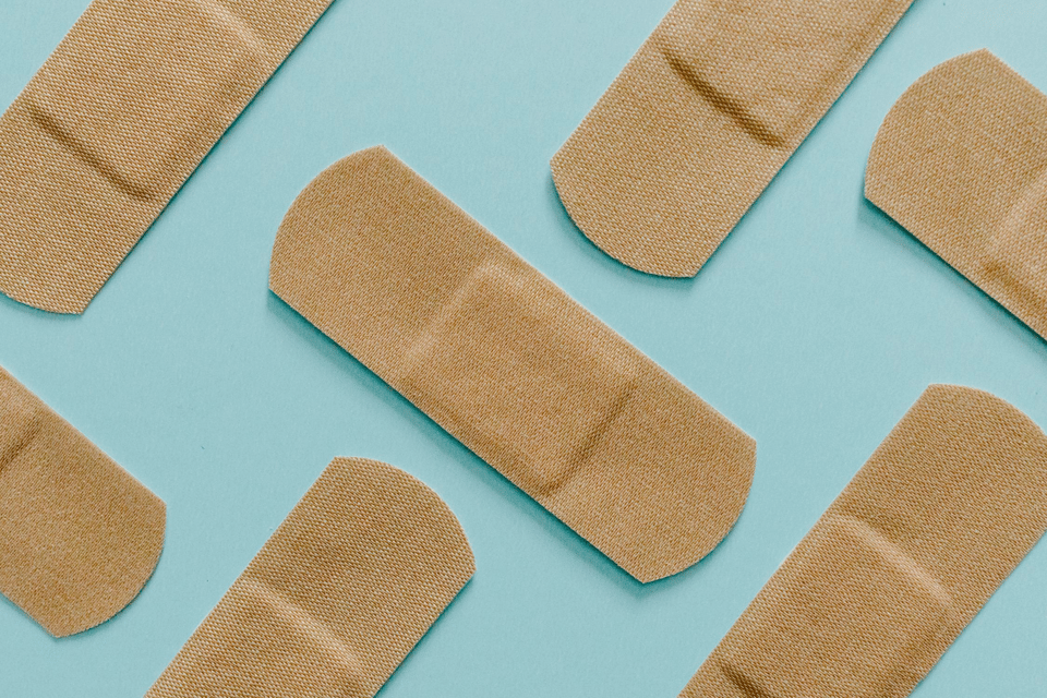 A photo of seven Band-Aids laid out in a zigzag pattern on top of a blue surface.