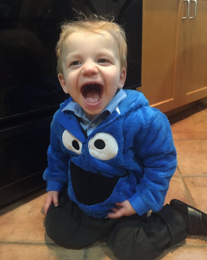 A happy toddler in a cookie monster sweatshirt on a kitchen floor