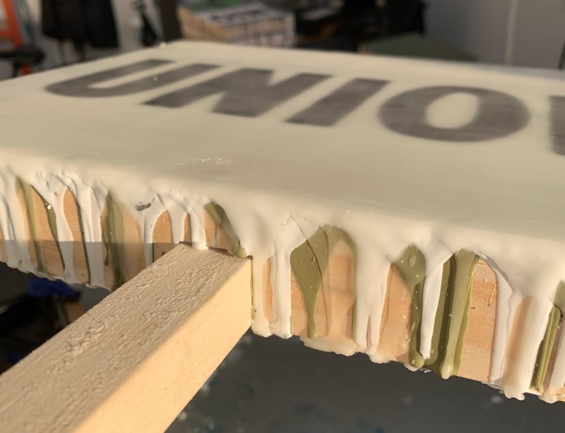 The bottom edge of a painting with lots of wax dripping off it, and a stick connected to the bottom.
