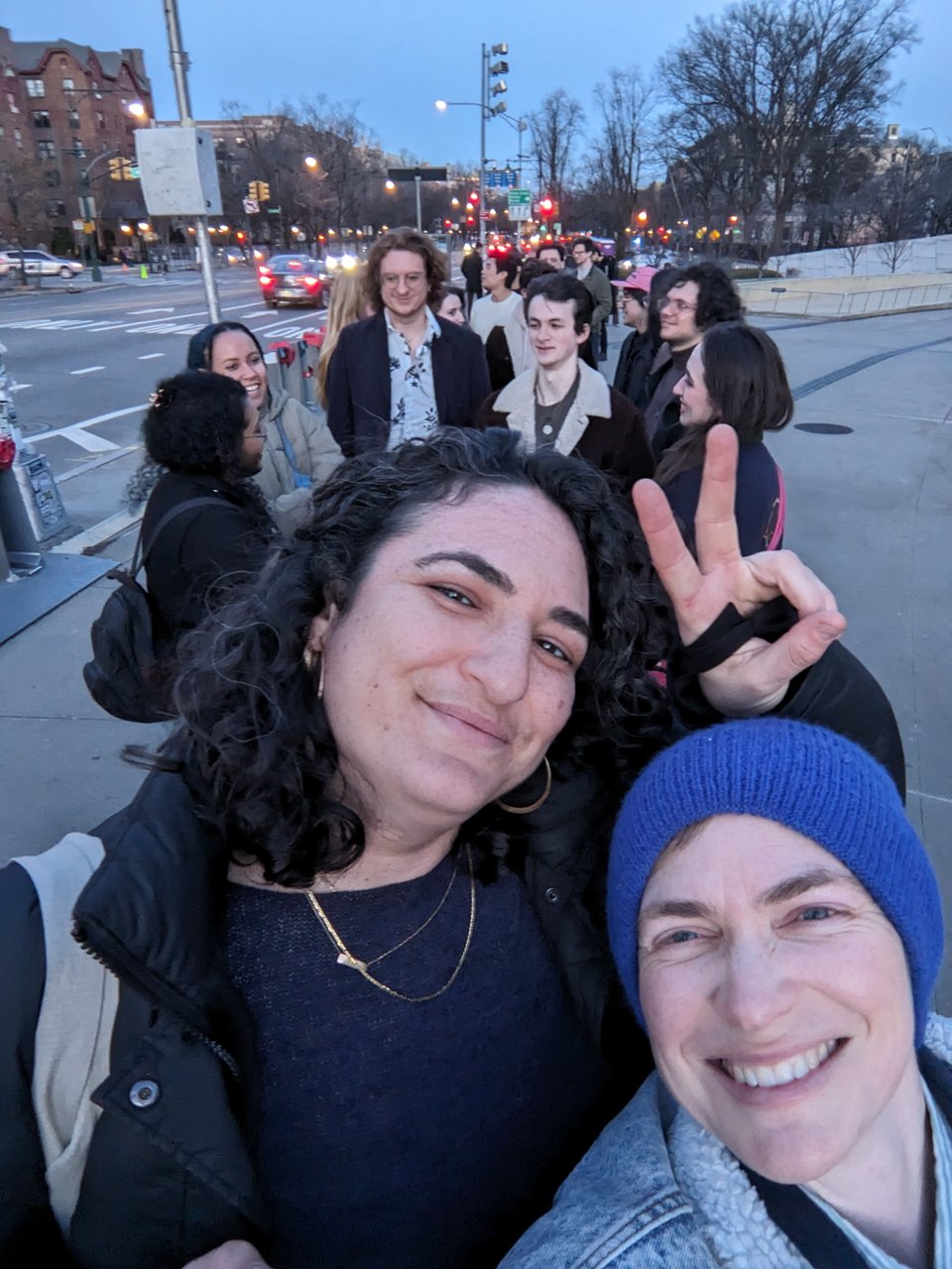 two people smiling as they stand in a line at sunset in central Brooklyn