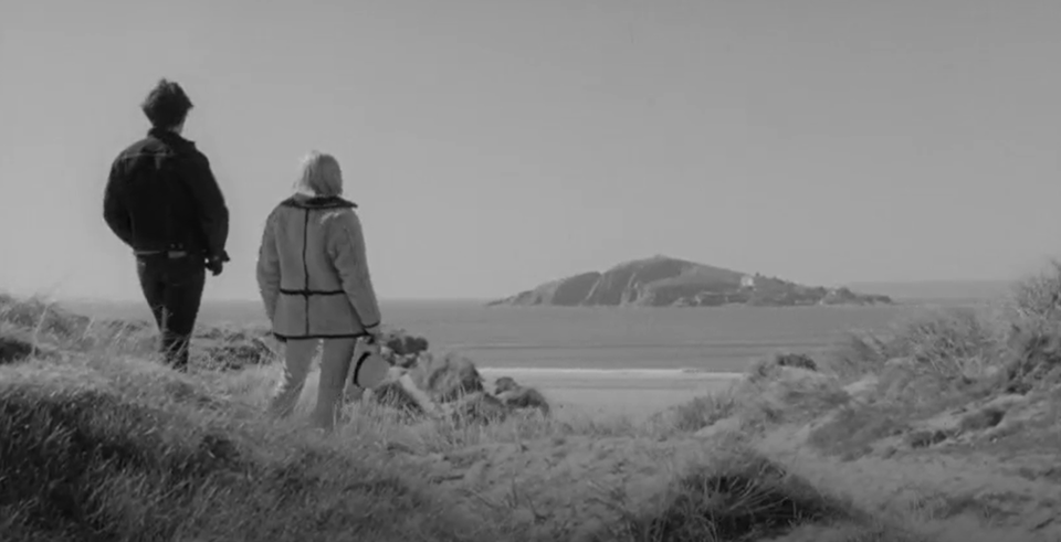 Steve (Dave Clark) and Dinah (Barbara Ferris) contemplate Burgh Island from the mainland. The hotel can be seen on it.