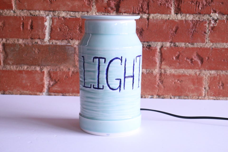 A light blue porcelain jar with a lamp cord coming out the back. The jar has a deep texture carved in, and the word 'light' in darker blue inlay handwriting.