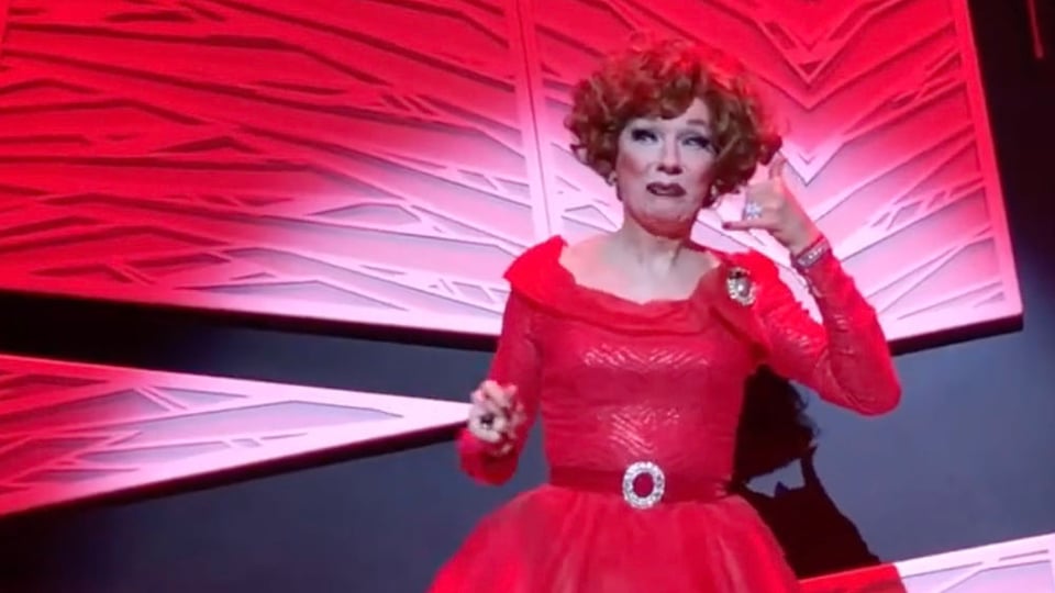 Drag artist Lipsynka, in a sparkling red gown against a red and black backdrop, mimes a telephone call in a performance of Sasha Velour's Nightgowns.