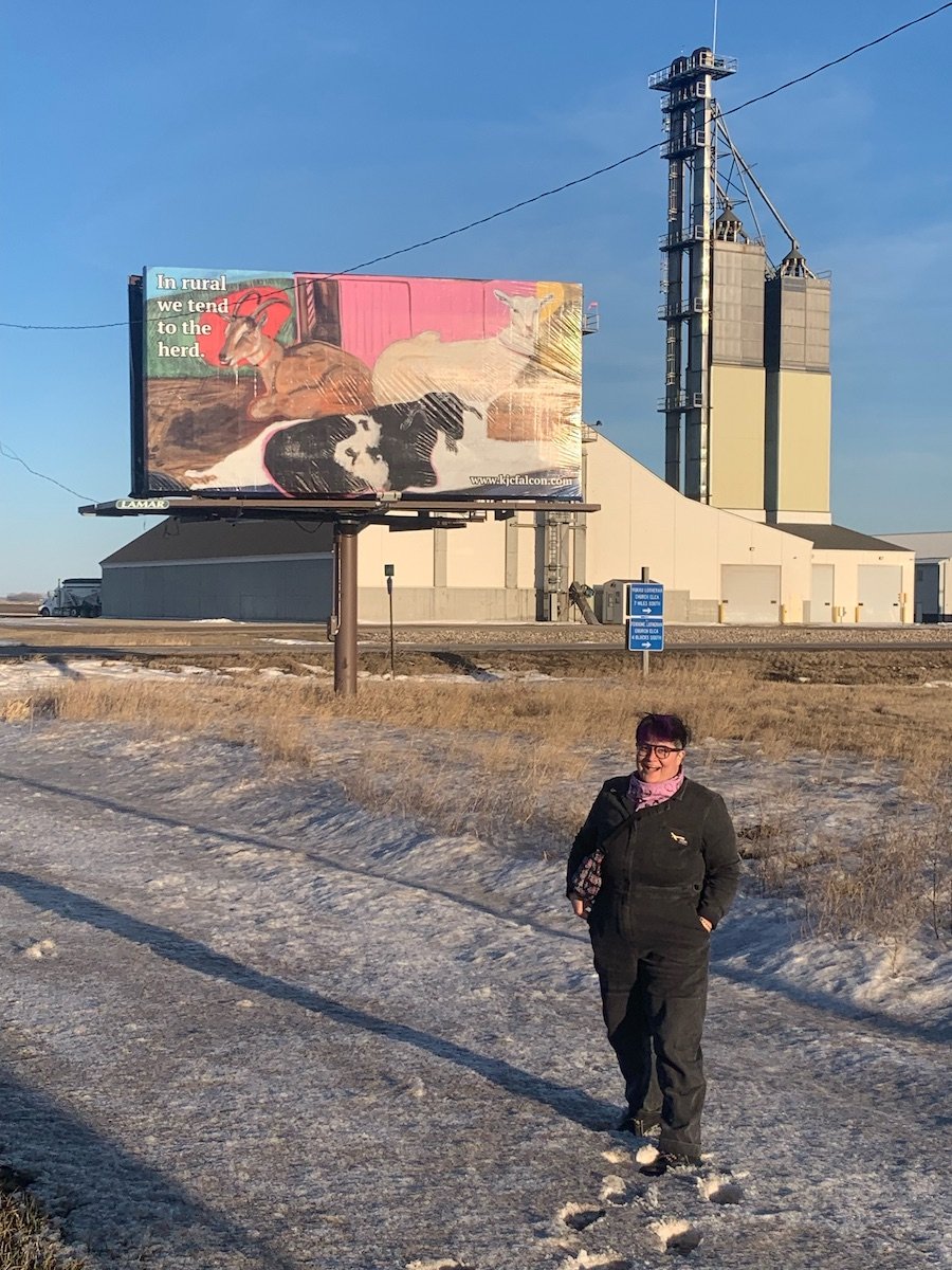 a chicanx artist in front a billboard featuring a painting of three goats