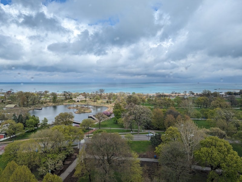 A sprawling green park with Lake Michigan in the background, underneath a blue sky with large patchy clouds
