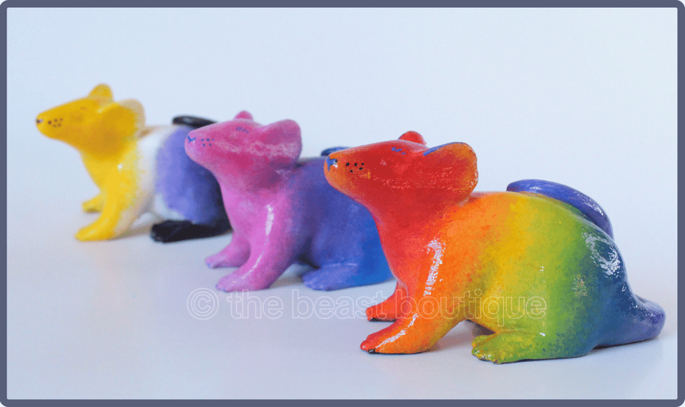 Three colorfully painted rats; the leftmost has colors from the Nonbinary flag, (yellow white purple black) the centermost with bi pride flag colors (pink purple and blue), and the rightmost rat which is closest to the viewer, with the Rainbow Flag colors.