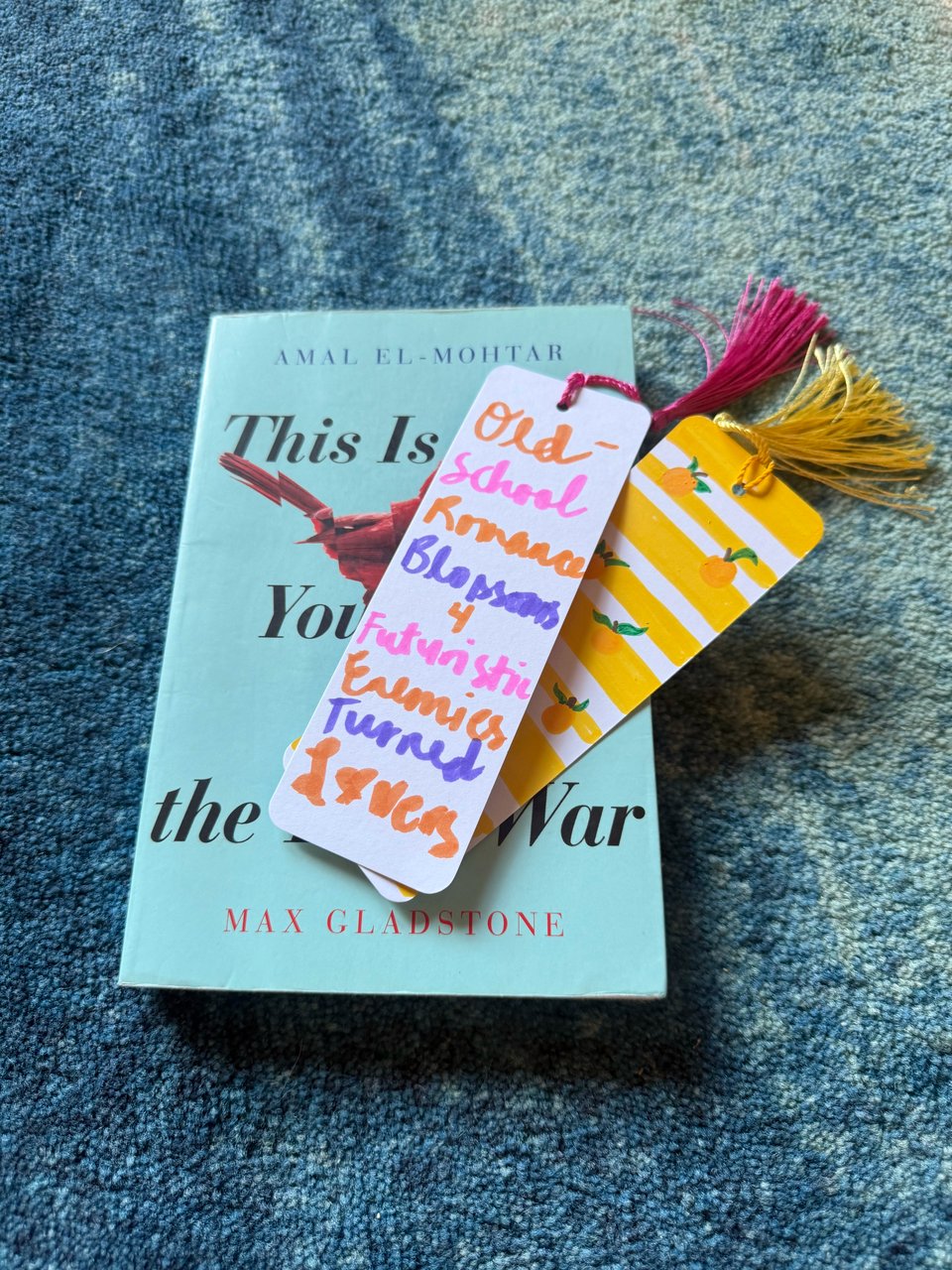 A book ("This Is How You Lose the Time War" by Amal El-Mohtar & Max Gladstone) with two handmade bookmarks, one with colorful handwritten text describing a romance trope.