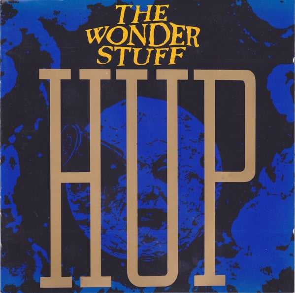 A still from the famous silent movie short, A TRIP TO THE MOON by Georges Méliès, showing a moon with a human face -- it's more like a human face that's been covered with cool whip -- with a bullet-shaped rocket sticking out of its eye. It has a kind of disgruntled look on its face. (Wouldn't you be?) This still is tinted blue, and "The Wonder Stuff" and HUP are superimposed over it.