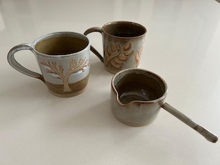Two pottery mugs and a pitcher, with tree and plant motifs