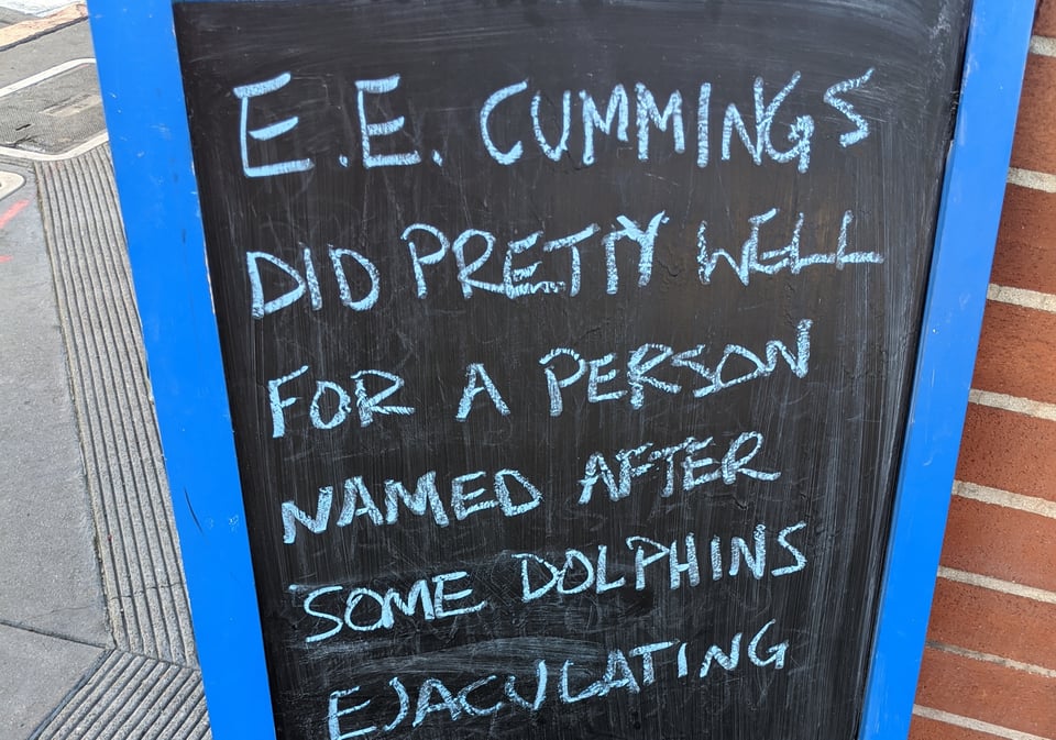 Chalk billboard reads E.E. CUMMINGS DID PRETTY WELL FOR A PERSON NAMED AFTER SOME DOLPHINS EJACULATING