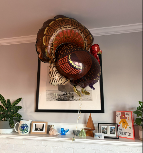 A large mylar balloon shaped like a turkey, floating over a mantel with some knick knacks on it
