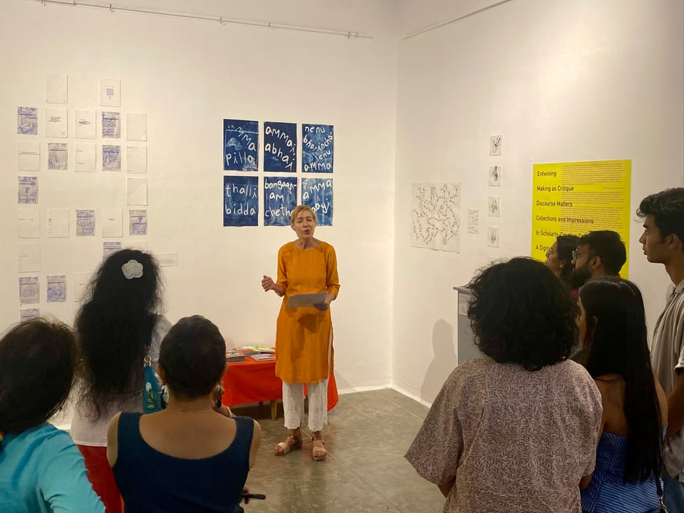A group of people in an art gallery with the exhibition curator offering her opening remarks.