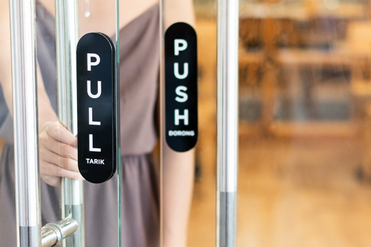 A close up of a pair of glass doors saying 'Pull' and 'Push' respectively. A feminine person is opening one of the doors.