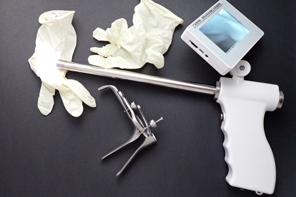 image of a veterinary tool featuring a camera to guide an insemination tube, lying beside a pair of latex gloves and a small duckbill speculum