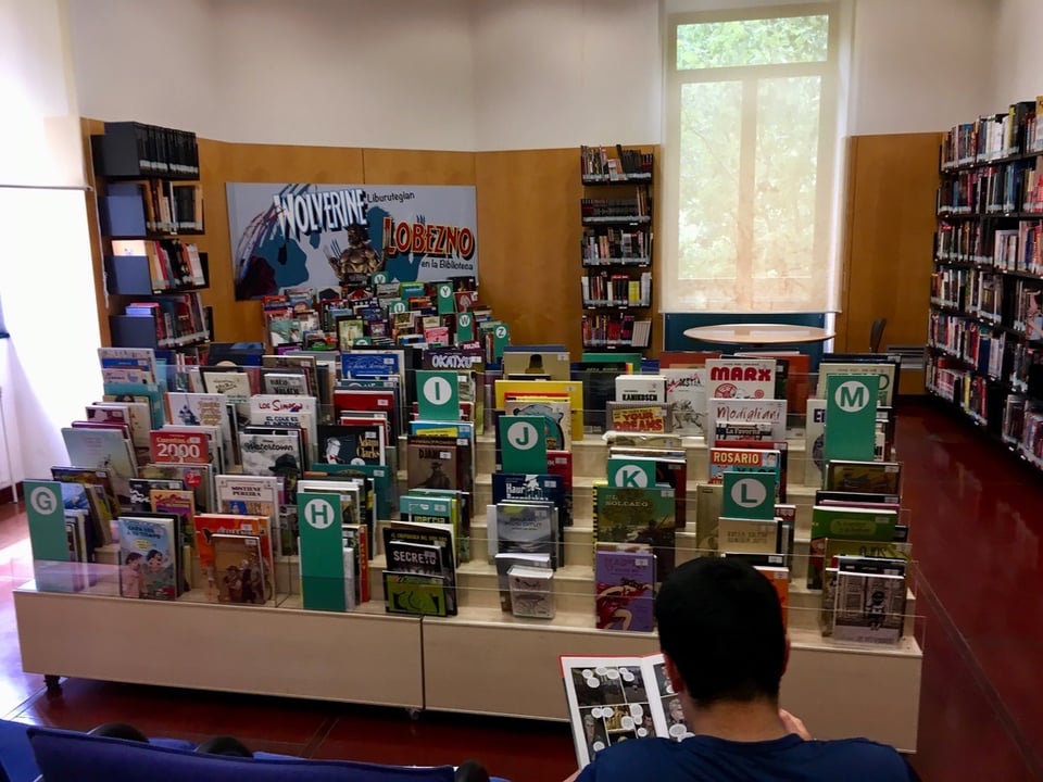In the foreground a person is reading a comic book in a room filled with comics.
