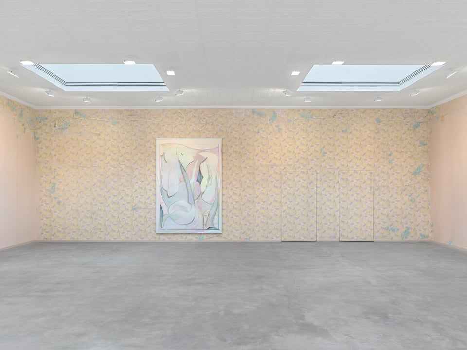 A gallery with a concrete floor and two skylights. A frontal view of the far wall shows an expanse of pastel wallpaper, hand detailed. A big abstract painting in a corresponding palette evokes a 1980s interior.