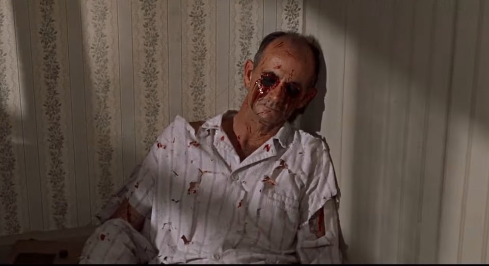 An older gentleman, now dead, is propped up in the corner of his bedroom, against some very pleasant wallpaper with vertical lines and floral vines. He is wearing shredded bloodstained striped pyjamas, has numerous wounds about the arms and face, and his eyes have been pecked out with fresh blood streaming down his cheeks.