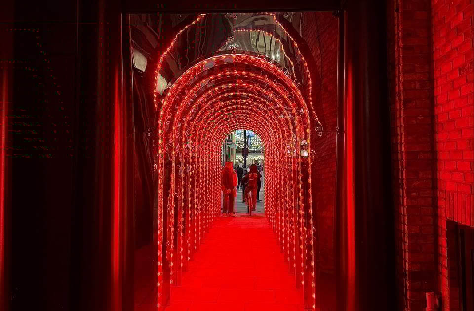 A small passageway tunnel that is bathed in red light strips going up and over and down one after another the whole length of the short tunnel.