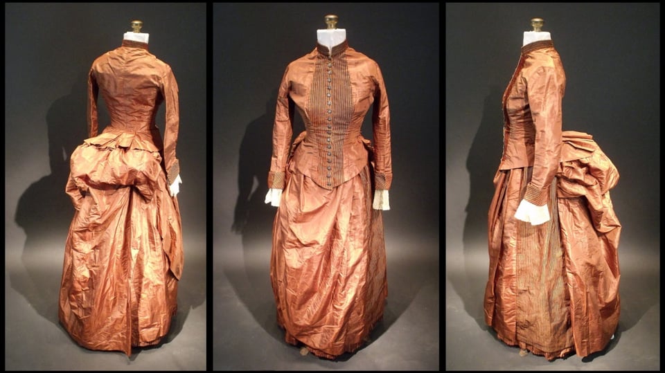 Three pictures of a copper colored vessel dress. On the left-hand side is a picture of the dress from behind, showing the big fluffy bustle. In the middle of a picture from the front, showing the long sleeves, slender, ending in a white raffle, and, dark piping going down the front of the chest. On the right is a sideways picture with the dress facing to the left.