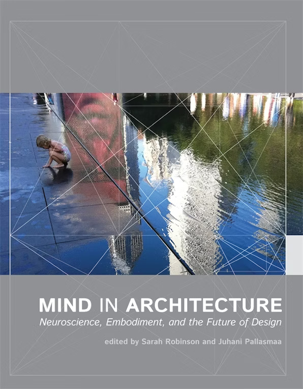 Book cover of “Mind in Architecture: Neuroscience, Embodiment, and the Future of Design,” edited by Sarah Robinson and Juhani Pallasmaa. The cover features a child bending down to touch the wet pavement at Crown Fountain in Chicago's Millennium Park, with reflections of buildings and a digital face display in the water. Geometric white linework overlays the image.