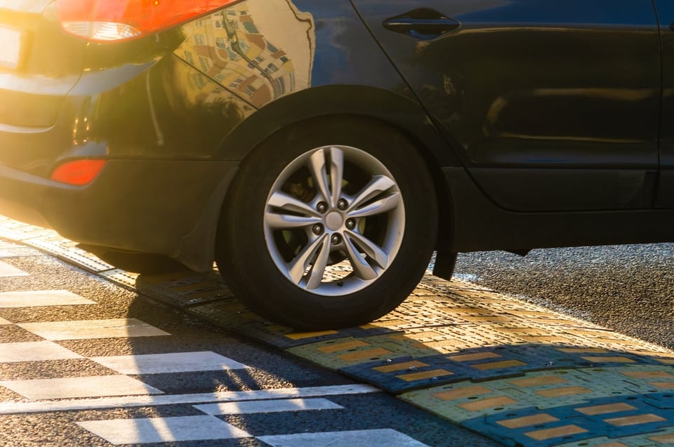 A close up of a car's rear wheels driving over a speed bump.