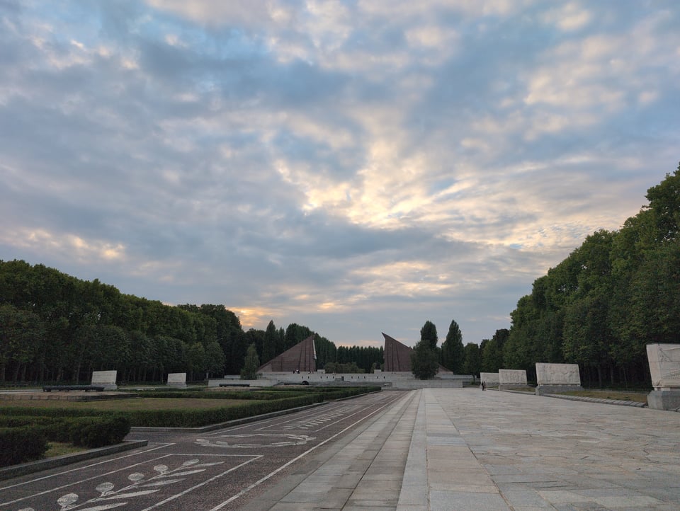 Sunlight filters through a mostly cloudy evening sky above the Soviet Memorial in Treptower Park.