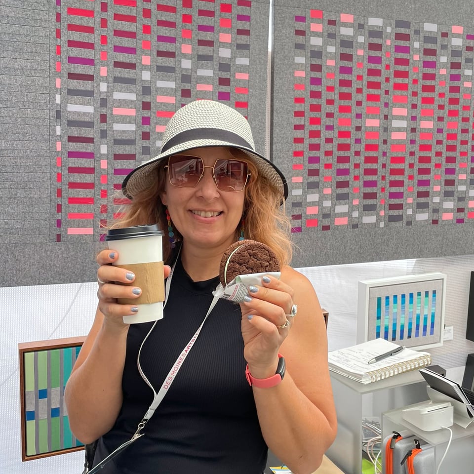 Mary Pow in front of her textile artwork with a coffee and an ice cream sandwich in her hands.