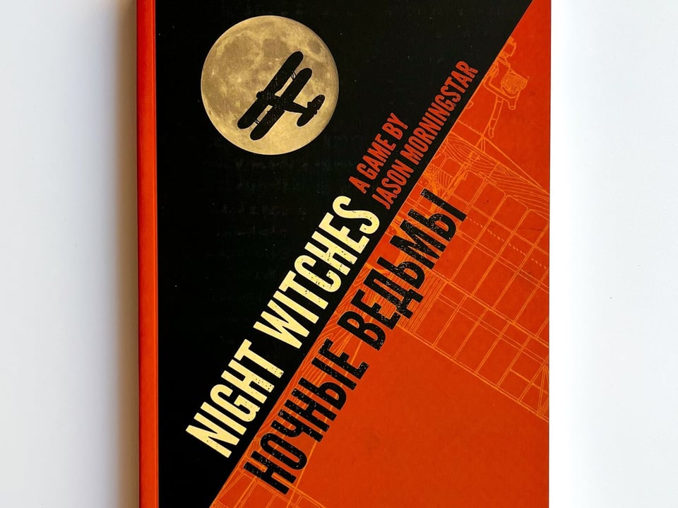 The cover of Night Witches, by Jason Morningstar. It features the title of the game in latin and cyrillic script, plus the silhouette of a biplane against the full moon.