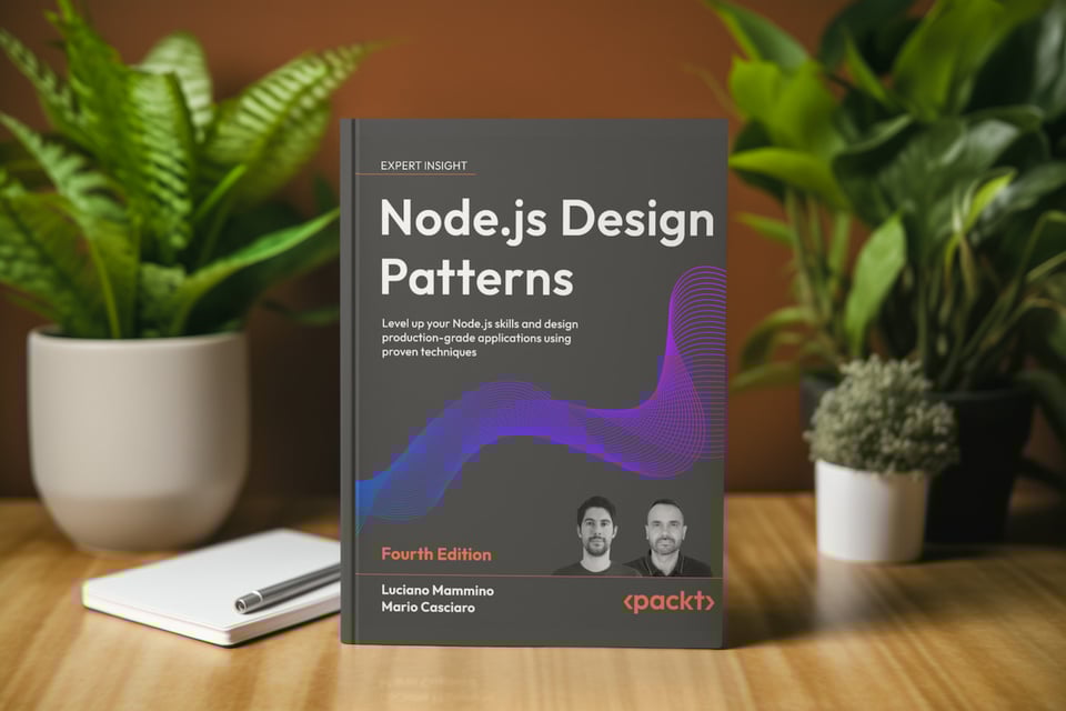 A hard cover copy of Node.js Design Patterns Fourth Edition stands on a wooden table with warm light, framed by green potted plants. The dark gray cover shows a purple and blue flowing wave graphic, the authors Luciano Mammino and Mario Casciaro with small portraits, and the Packt logo. A white notebook and pen rest to the left.
