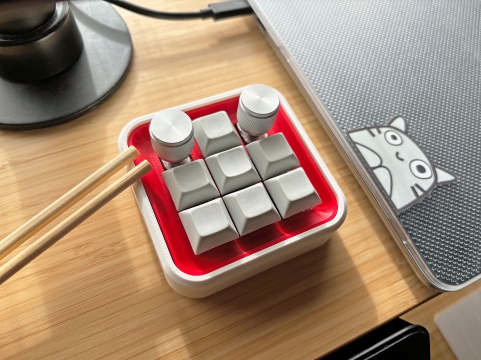 Photo of the Banchan macropad, a 3x3 key macropad with a white case and red plate