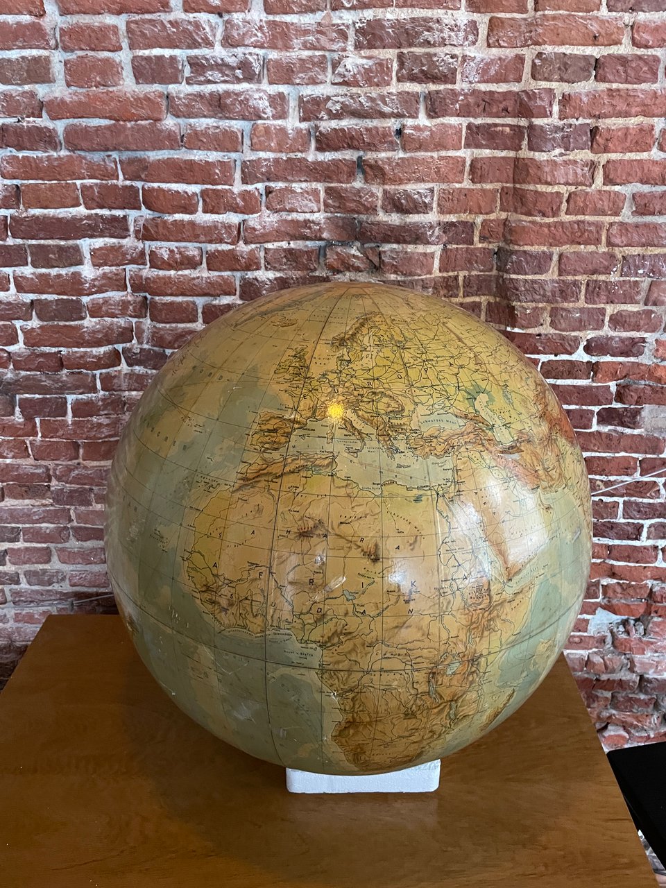 A large antique globe sits on a table in front of a brick wall.