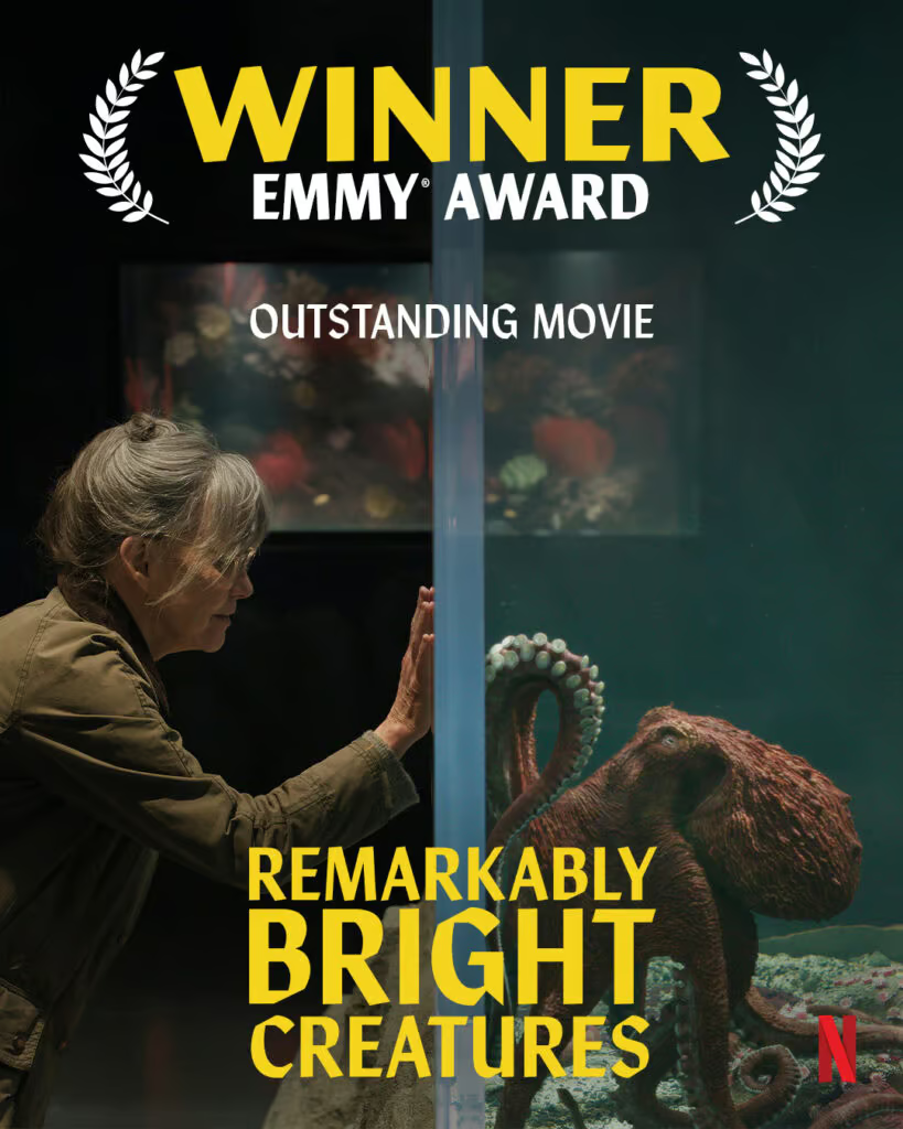 Promotional poster for Remarkably Bright Creatures winning an Emmy Award for Outstanding Movie. The image behind the words is an old woman on the left and a (CG) octopus on the right both reaching toward the wall of an aquarium that divides the image down the center.