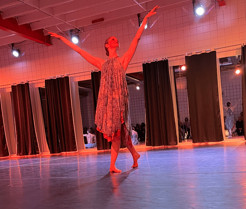 A woman in a flowing dress lifts her arms high in mid-movement during a dance performance