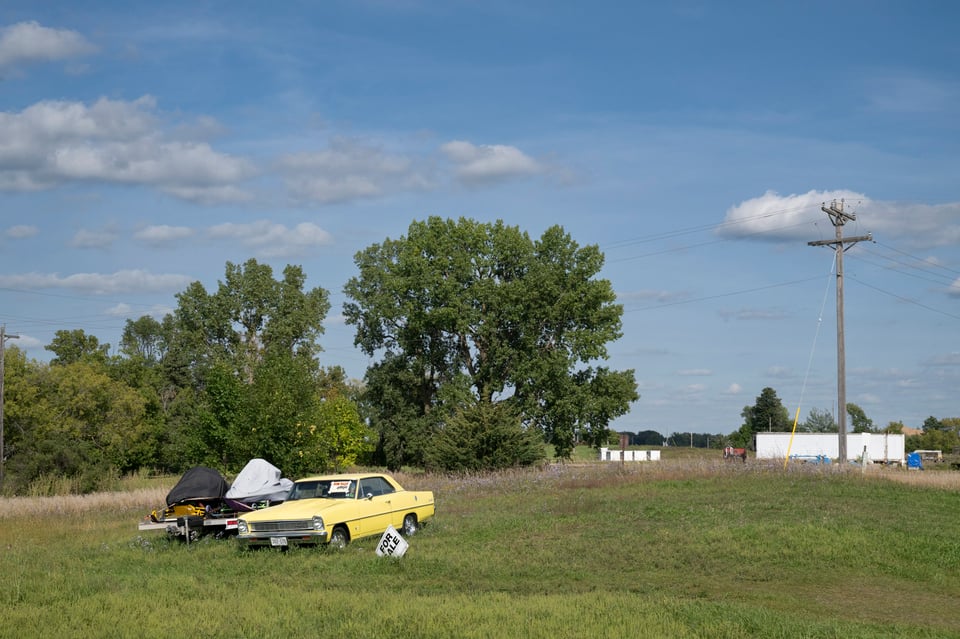 Photo of a car and two covered jet skis with a for sale sign in front of them.