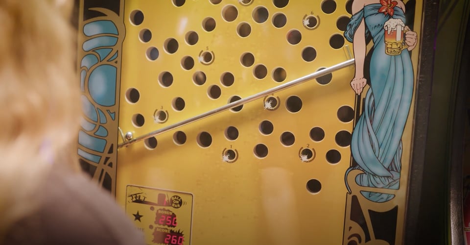 A woman plays Ice Cold Beer by moving a metal bar up a playfield.