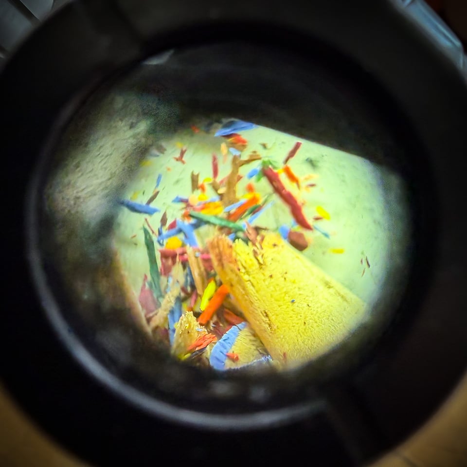 A colorful assortment of pencil shavings and small debris is viewed through a circular lens.