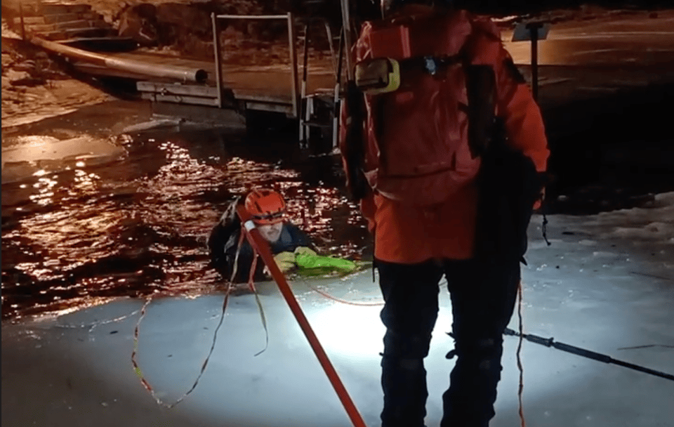 A guy in a hole in ice holding a throwline bag.