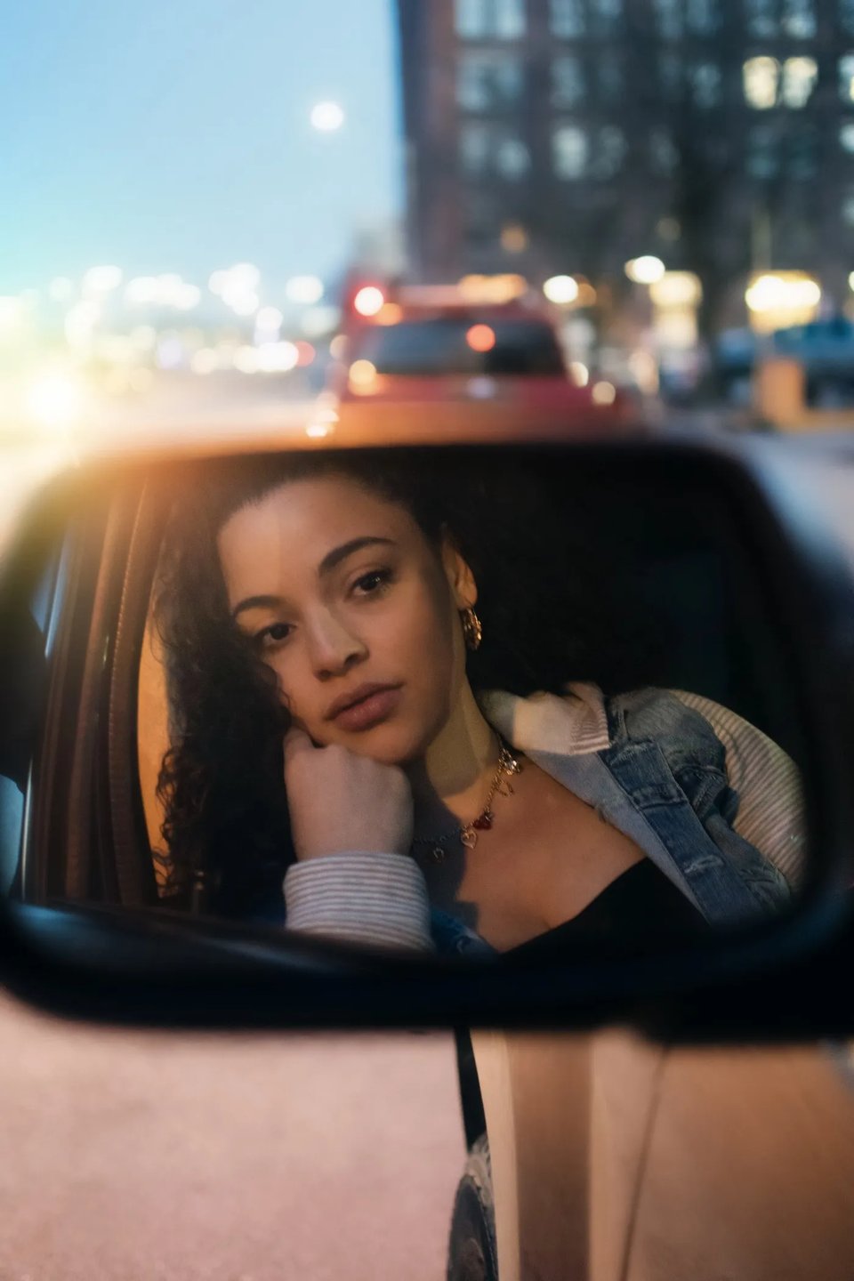 a young woman looking at herself in the rear view mirror of a car