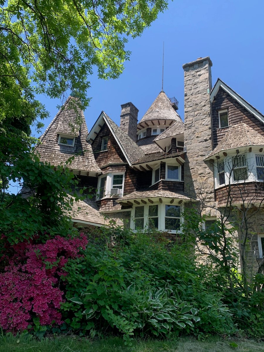 A large stone and shingle mansion surrounded by greenery