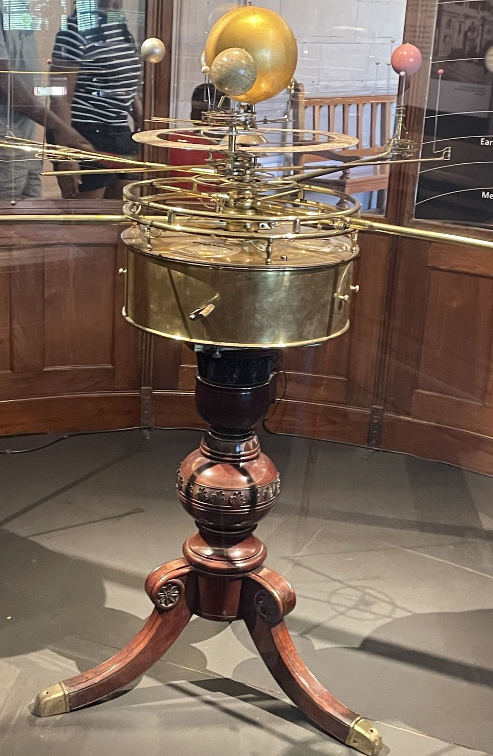 Picture of an Orrery: a mechanism made of brass demonstrating the inner planets orbiting the sun, all supported on three carved wooden legs also tipped with brass.