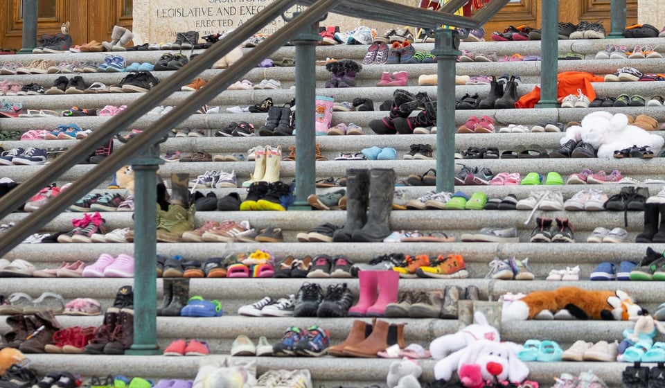 A photo of a flight of stairs covered with different pairs of childrens footware, as well as a few stuffed toys, to honour the Indigenous children lost to Residential schools.
