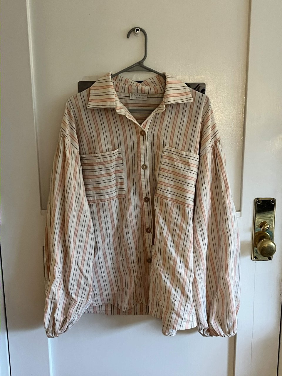 A pink white and grey stripped linen shirt hanging on a hanger, front on.
