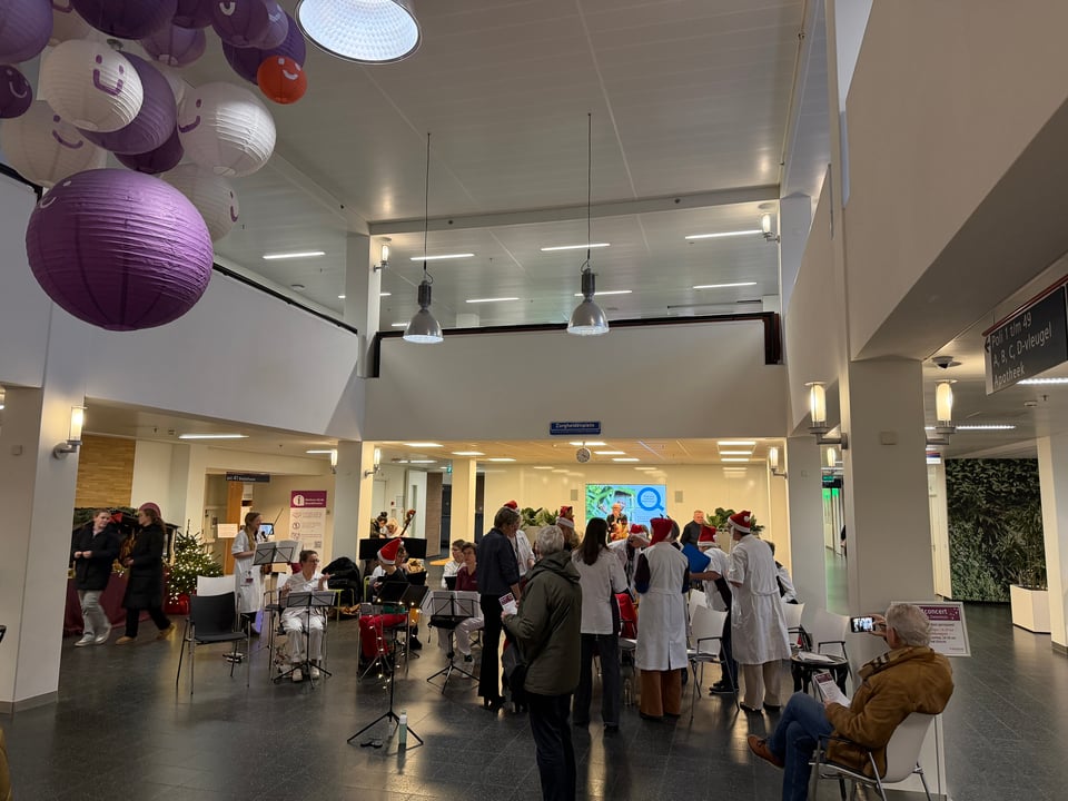 A group of medical staff prepare for a musical Christmas concert in the lobby of a hospital.